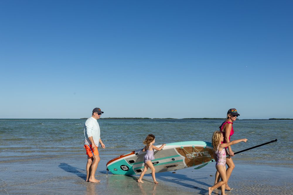 Guests carrying a paddleboard across the sandbar