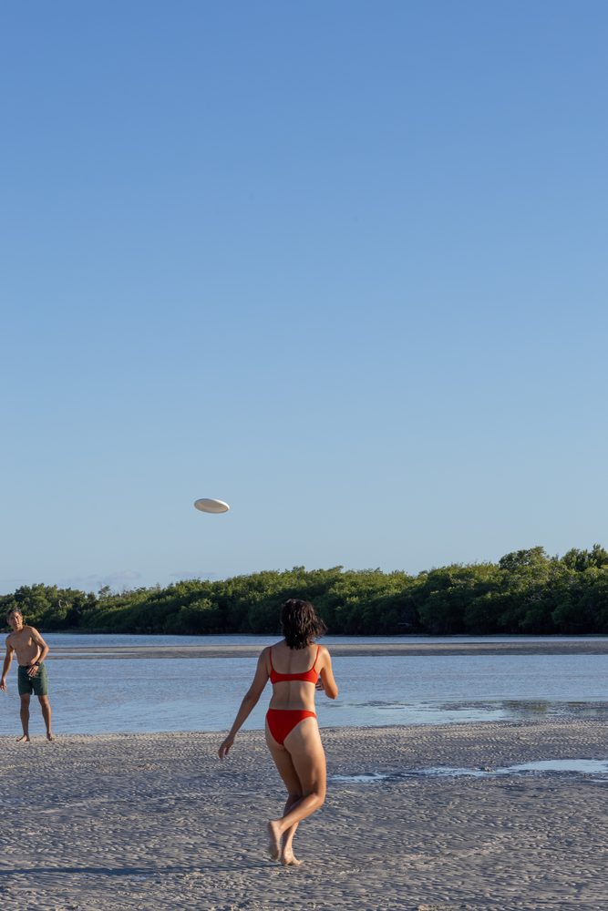 A guest throwing a frisbee on the sandbar beach beside a mangrove island