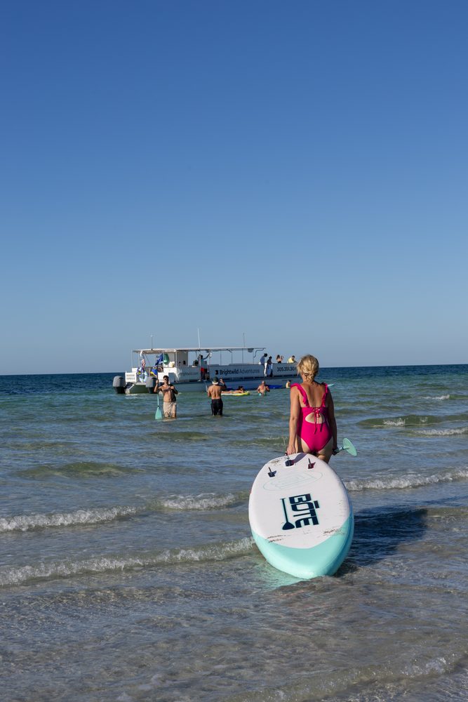 A girl on a paddleboard with the Brightwild boat behind her