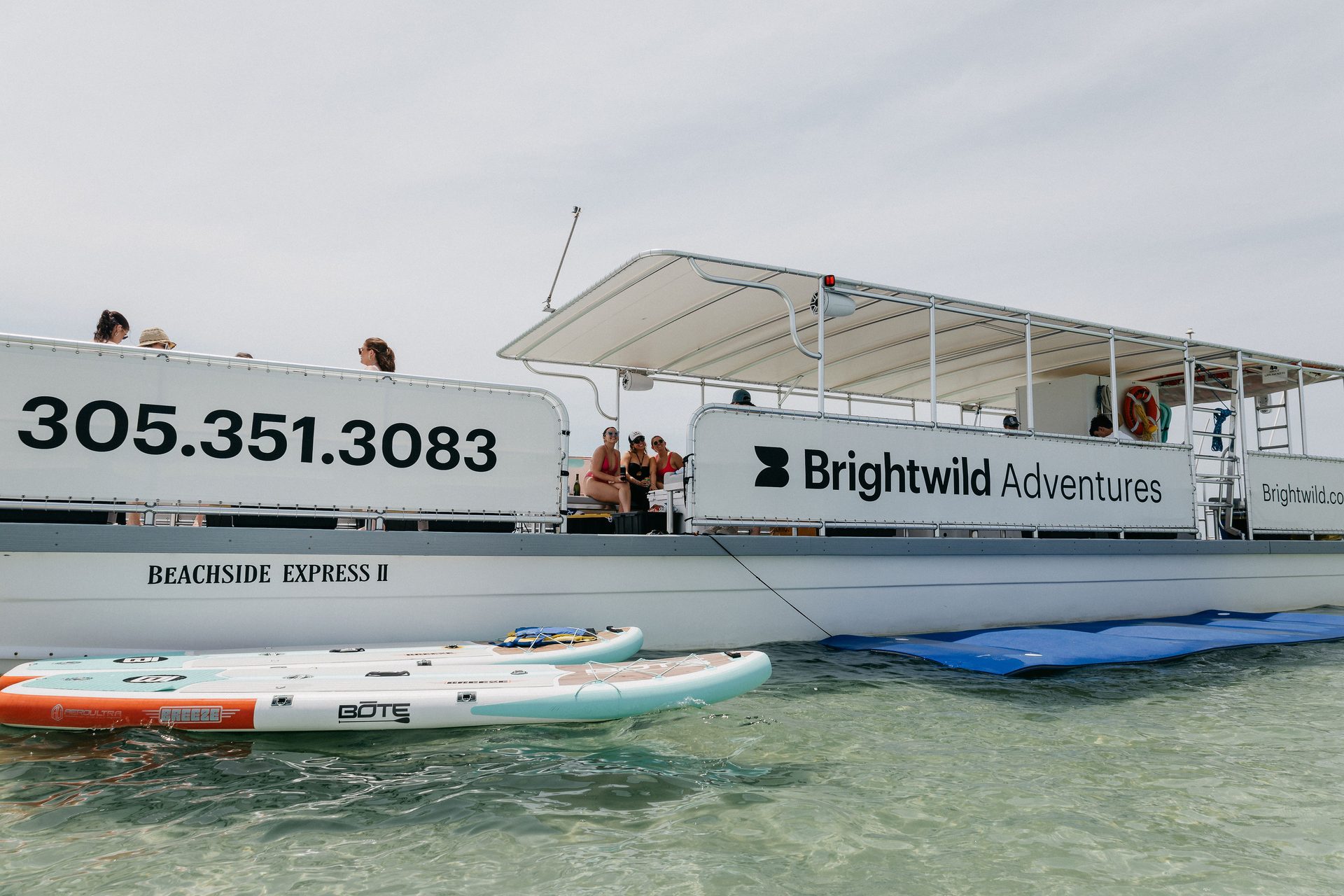 The Brightwild Adventures boat anchored on the sandbar with paddleboards floating alongside